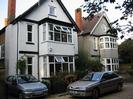 Two houses with large bay windows.
Both have small windows on the gable-ends: the left-hand one is square, the right-hand one is octagonal.
Parked cars.