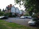 Large house now used as offices: red brick, white timbers, dark tile roof with brick chimneys.
Car park with overhanging trees.