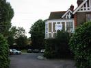 Small car-park set between trees and house.
Large house on right now used as offices - sign on wall says "MaST"
Lower floor of house obscured by bushes.
Upper floor has pebbledash between white-painted timbers.
Dark tile roof.