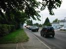 Road with pavement, grass, and hedge on left, with overhanging trees.
Roadsign warning of roundabout ahead.
Queue of cars passing over Maidenhead Bridge in the distance.
Boarded-up hotel (Skindles) on the right.