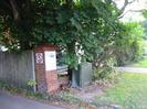 Red brick pillar with signs: 5mph speed limit and "MaST Consultancy & Training HERMITAGE HOUSE"
Green roadside cabinet.
Trees.