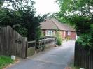 Danehurst.
Concrete driveway with wooden slat fences.
Decorative stone balustrade on far side of driveway.
Red brick bungalow with brown tile roof.