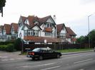 Looking across the A4 Bath Road at a group of three-storey houses on the corner of Ellington Road.
Houses have white-painted walls with some black timbers and some tile-hung areas.
The corner house has a round window at first-floor level.