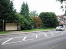 Road with bus-shelter and bank of small trees on far side.
30mph speed-limit sign and house on far right.