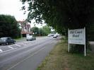 Looking west on the A4 Bath Road.
Three-storey house on far side of road.
Sign for Old Court Hotel on right under large trees.
Cars on road.