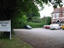 Old Court Hotel car-park.
Hotel sign under trees on left.
Cars and vans parked around hotel building on right.