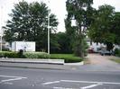 The entrance to Norfolk House Hotel.
Low wall with hedge along road.
Hotel sign and flagpoles.
Grassy area with trees.
Gravel drive and car-park.
White two-storey hotel building with dark slate roof.