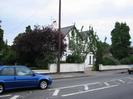 White house with dark slate double-pitch roof.
Low wall along road with trees and shrubs behind.
Telephone pole.