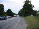 Looking west on the A4 Bath Road.
Walls and trees on the left, with houses just visible behind.
Pavement and scrubby verge on right.
Bank of dark trees.
Part of hotel building visible on extreme right.