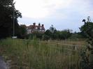 Scrubby verge with wooden fence and street light.
Trees with red-brick hotel building beyond.