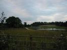 Wooden fence and regenerating undergrowth around the Jubilee River.
Wooden footbridge in the distance.
Roofs and chimneys of Taplow Court visible on the skyline.