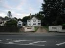 Kanellan: two-storey white house with asymmetrical pitched roof.
Low white walls each side of gravel driveway.
Large trees on the right.