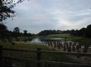 The Jubilee River.
Wooden post-and-rail fence in the foreground.
Newly-planted trees in protective containers.
Footbridge in distance.
Chimney of Taplow Paper Mill visible on skyline at left, roofs and chimneys of Taplow Court on skyline to the right.