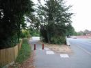 Tarmac footpath with bollards leading to footbridge across the Jubilee River.
Road bridge on right.
Wooden slat fence.
Trees.
Houses visible on right above parapet of bridge.