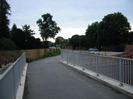 Pedestrian bridge across Jubilee River.
Galvanised metal railings on each side.
Wooden slat fence on left of path beyond bridge, with trees behind.
Traffic and traffic lights on A4 in the background.