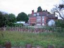 Hotel building of three storeys in red brick with strong horizontal features in white.
Red tile roof with dormer windows.
Gravel carpark.
Scrubby area in foreground with newly-planted trees.