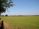 Large grassy field with houses and farm buildings in the distance.