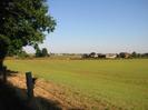 Large grassy field with houses and farm buildings in the distance.
