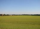 Large grassy field with houses and farm buildings in the distance.