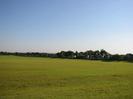 Large grassy field with houses in the distance.