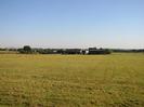 Grassy field with farm buildings on the far side.