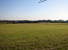 Grassy field with trees and farm buildings in the distance.