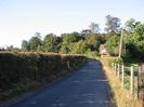 Looking north on Hitcham Road.
High hedge on left, barbed-wire fence on right.
House in distance at bend in road.