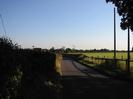 Looking south on Hitcham Road.
High hedge on left.
Fence and field on right.
Houses visible in the distance.