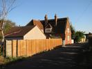 Looking south on Hitcham Road.
High wooden fence on the left with red-tile roof seen beyond it.
Unusual red-brick and tile house: The Old Reading Room, with two tall chimney stacks.