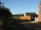 Looking north on Hitcham Road.
High hedge on the left.
Fence and hedge on the right.
Garage behind fence has pink end-wall and dark red tiles.
Corner of red-brick house on far right.