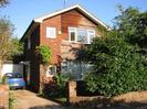 Low brick wall with house and bush behind.
Left side of house in reddish brick. Right side in brown weatherboards.
White window-frames.