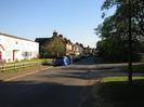 Looking south on Hitcham Road.
Row of white terraced houses on the left with grass and low fence in front.
Red brick houses in the distance.
Grass verge on right.
