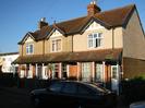 Terrace of three houses.
All have pebbledash rendering on first floor level, and red tile roofs.
Tiled porch runs the full length of the terrace at the front, linking bay windows,
and with white supporting posts.