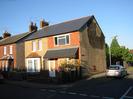 Pair of houses with grey tiled roof.
Left hand house has pebbledashed walls and white window frames.
Right hand house is boarded up and has render missing from the end wall.