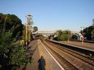 Railway platform with red lamp-posts.
Covered iron footbridge crosses to island platform on right and also to far side of main line.
Station buildings beyond bridge.