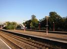 Railway platforms with footbridge and red lamp-posts.
Sign on lamp-post: TAPLOW
Small tree on island platform.
Large trees on far side of railway.