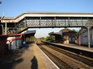 Railway platform with red covered bike stand.
Covered iron footbridge with inset GWR logos and lattice sides.
Station buildings with canopies beyond footbridge.