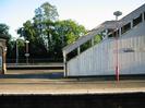 Island platform with white boarded steps leading to footbridge.
Red lamp-posts.
Iron railings and trees on far side of main line.