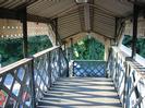 Northern end of footbridge.
Corrugated metal roof with decorative wooden boarding each side.
Iron lattice bridge structure
Strong shadows across bridge deck caused by low sun.