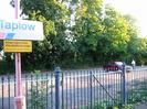 Blue-painted iron railings and gate.
Red lamp-post with signs: "Taplow", "Keep back from platform edge. Passing trains cause air turbulence".
Car-park with large trees beyond.