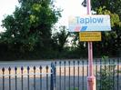 Blue-painted iron railings.
Red lamp-post with signs: "Taplow", "Keep back from platform edge. Passing trains cause air turbulence".
Car-park with large trees beyond.