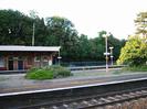 Island platform seen across main line.
Station buildings on far platform.
Railings with road and trees beyond.