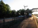 Platform 1.
Blue and white iron railings with car-park and trees beyond.
Lamp-post and camera pole.
Footbridge on right.