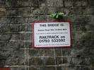 Brick wall with sign:
"THIS BRIDGE IS: Station Road 22m 31.25ch MLN. If you witness a vehicle striking this bridge contact RAILTRACK on 01793 533592 as quickly as possible. The safety of trains may be affected"