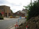 Road with buildings on the far side, and roadworks in progress.