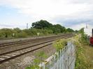 Railway tracks with trees on the far side.
Metal fence on right.