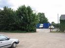 Car-park with entrance to works yard.
Blue shipping containers in yard.