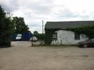 Car-park and entrance to works yard.
Vehicles and blue shipping containers in yard.
Low white building on right with grey slate roof.