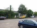 Car park with cars.
Low building with grey slate roof.
Small trees.