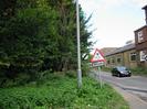 Road with trees and scrub on left, buildings on right.
Street-light pole and height-limit sign.
Signs for national speed limit.